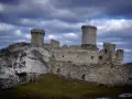 Ruiny zamku Ogrodzieniec na skale, z wieżami i murami, pod burzowym niebem. Idealne miejsce na trasę pełną historii.