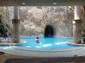 Relaks w basenach w jaskiniach. Mężczyzna wchodzi do turkusowej wody, a za nim widać skalne ściany i wejście do kolejnej groty.