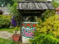 Kolorowa studnia z ludowymi wzorami kwiatowymi, otoczona zielenią i krzewami róż. Idealne miejsce na wakacje na wsi.