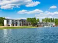 Nowoczesny Tiffi Hotel Olsztyn nad jeziorem, z łodziami przy pomoście i zielenią.