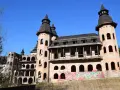 Niedokończony zamek z cegły z wieżami i graffiti na tle błękitnego nieba.