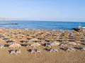 Plaża sol marina beach crete z rzędami leżaków i parasoli, gotowa na gości. Błękitne morze i niebo tworzą idealne tło.