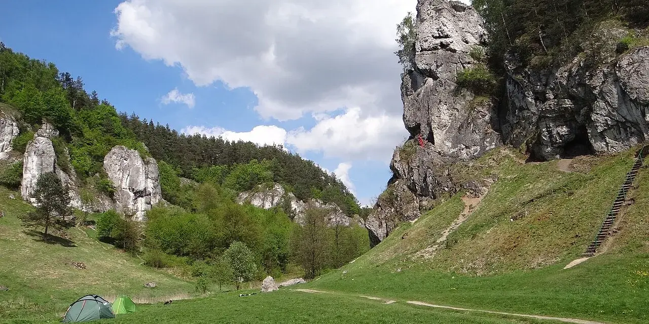 Zielona polana w Dolinie Kobylańskiej, namioty i skalne ostańce. Szlaki turystyczne prowadzą przez malownicze tereny Jury.