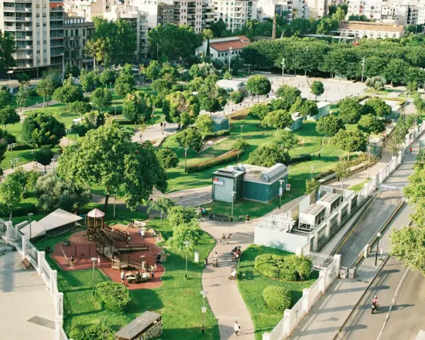Park z placem zabaw i alejkami, otoczony budynkami. Wygląda jak jeden z najbardziej zielonych miast w Polsce.