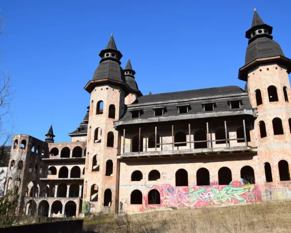 Niedokończony zamek z cegły z wieżami i graffiti na tle błękitnego nieba.